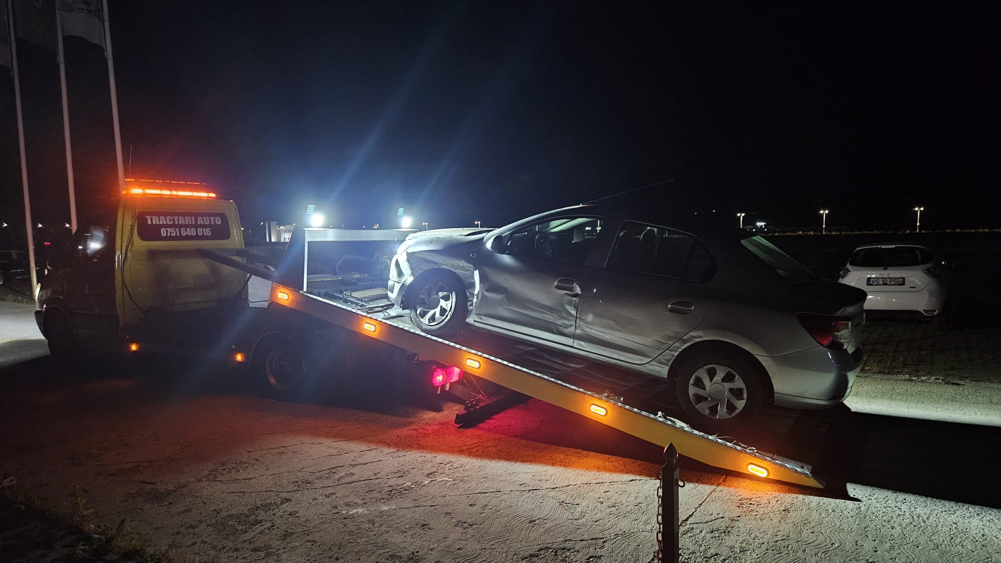 Dacia Logan avariata in partea stanga fata, incarcata pe platforma Traian TKD pe timp de noapte.
