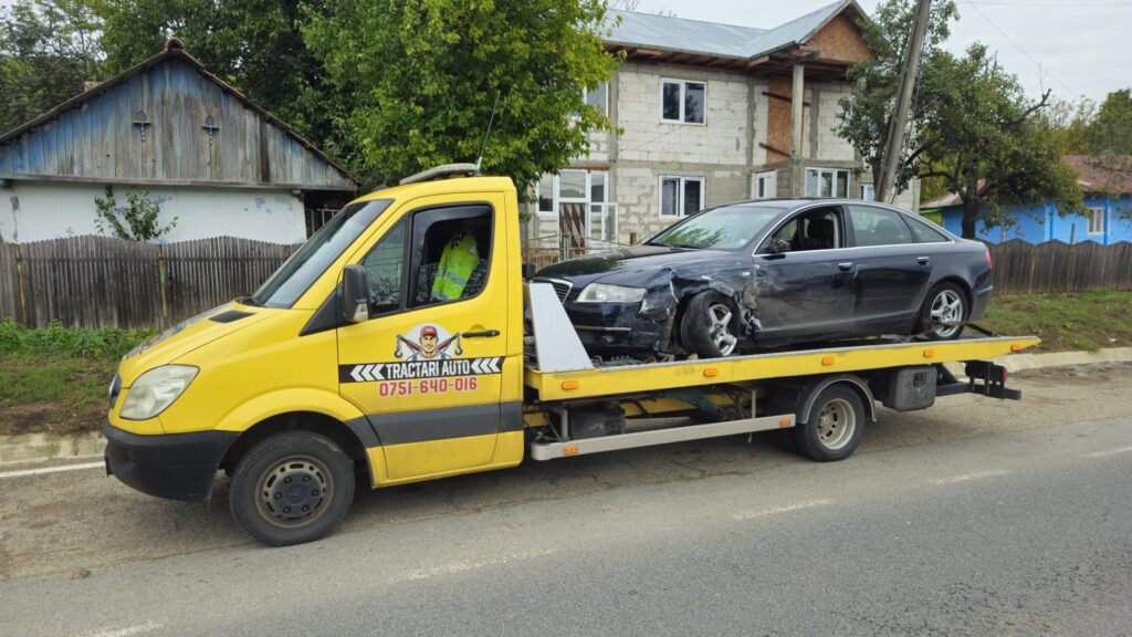 Autospecială galbenă Traian TKD Tractari Auto Iași efectuând o tractare dupa accident iasi pentru un autoturism Audi A6 negru, avariat frontal și securizat pe platformă.